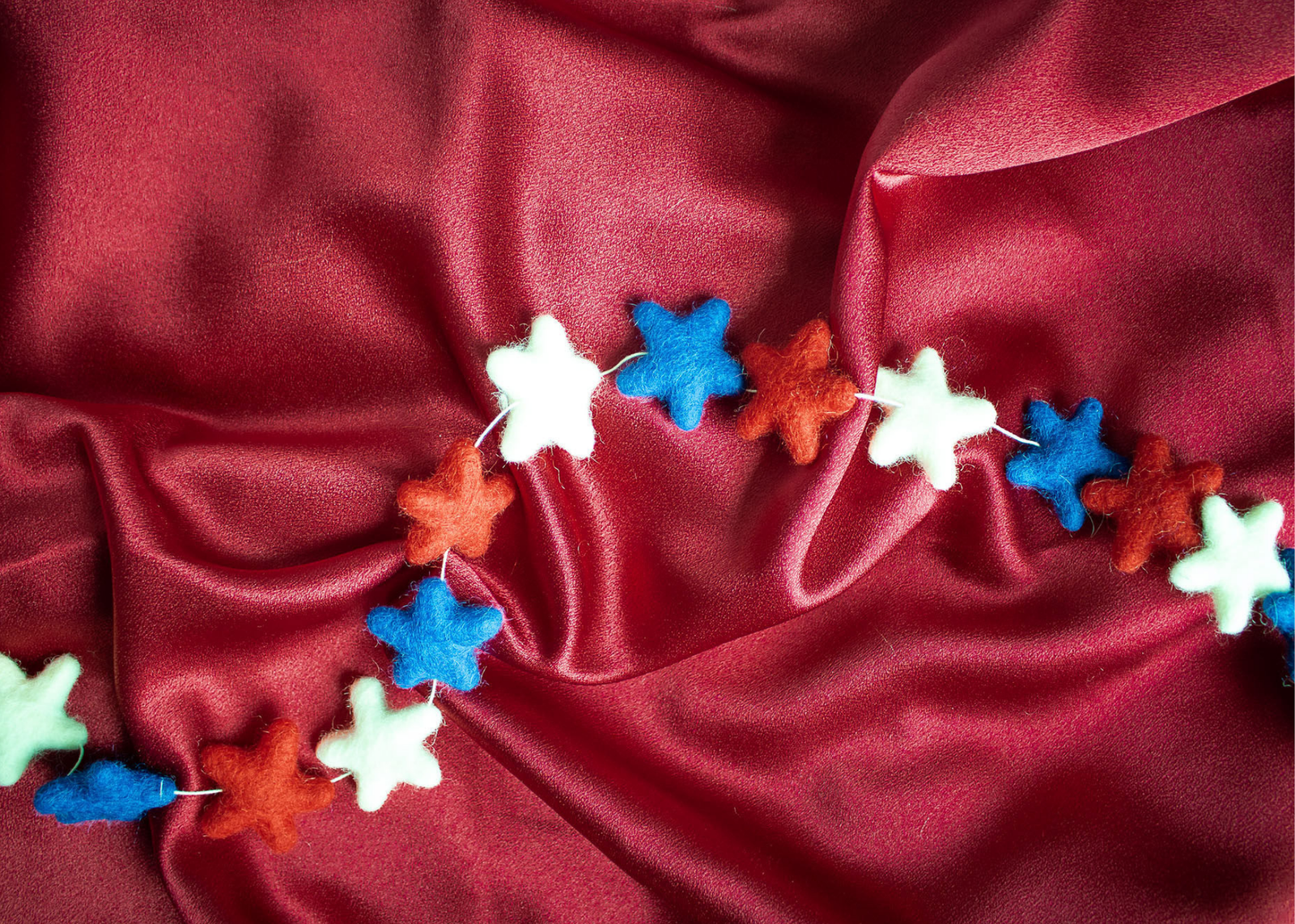 a red white and blue wool star garland lays on red silk fabric