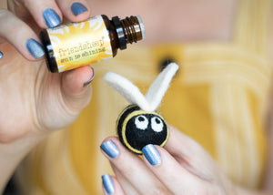 Sun is shining essential oil being dropped on a bee eco freshener made of wool. The bee is black and yellow with white wings and googley eyes