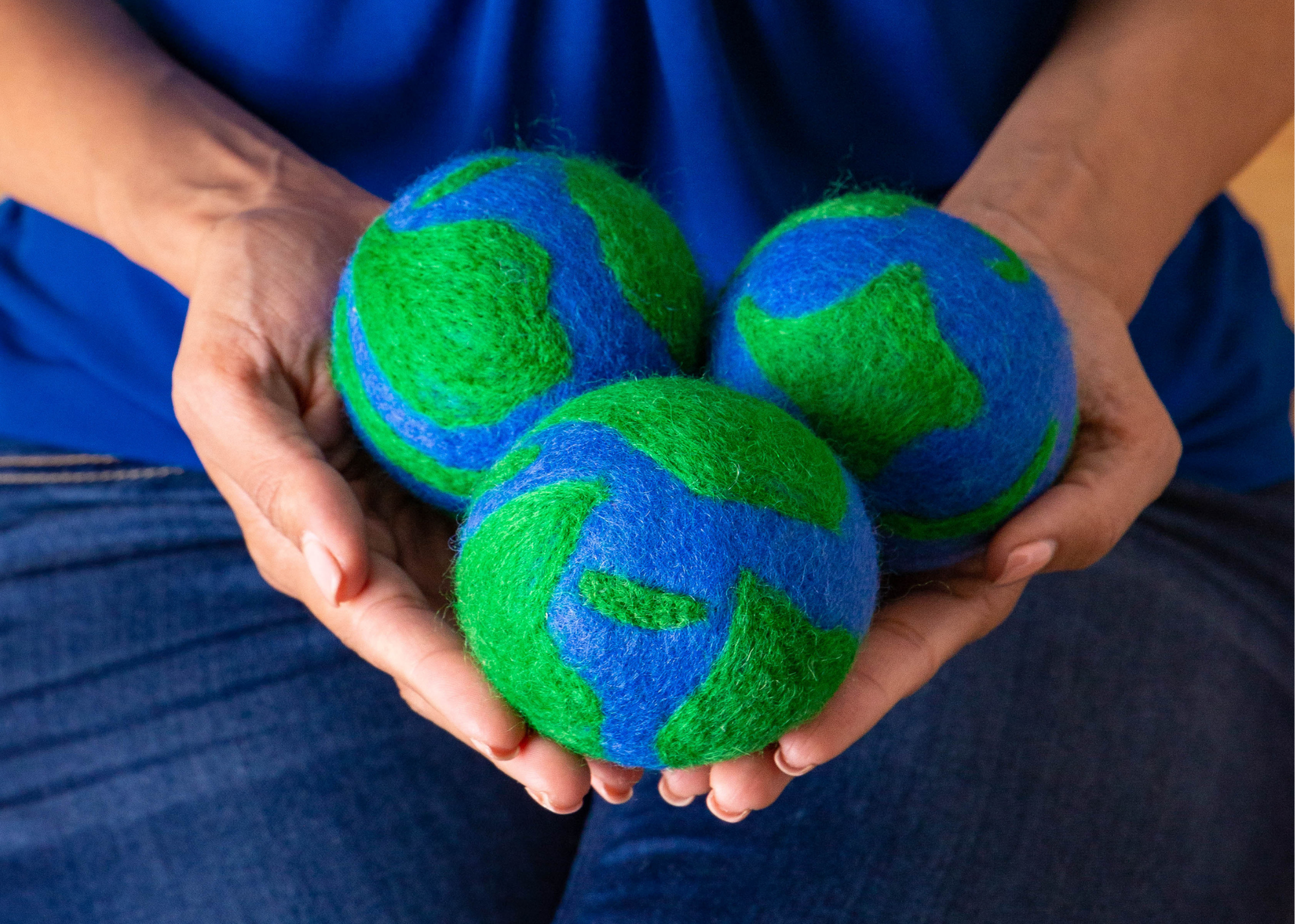 a person holds 3 green and blue Earth patterned wool dryer balls in their hands