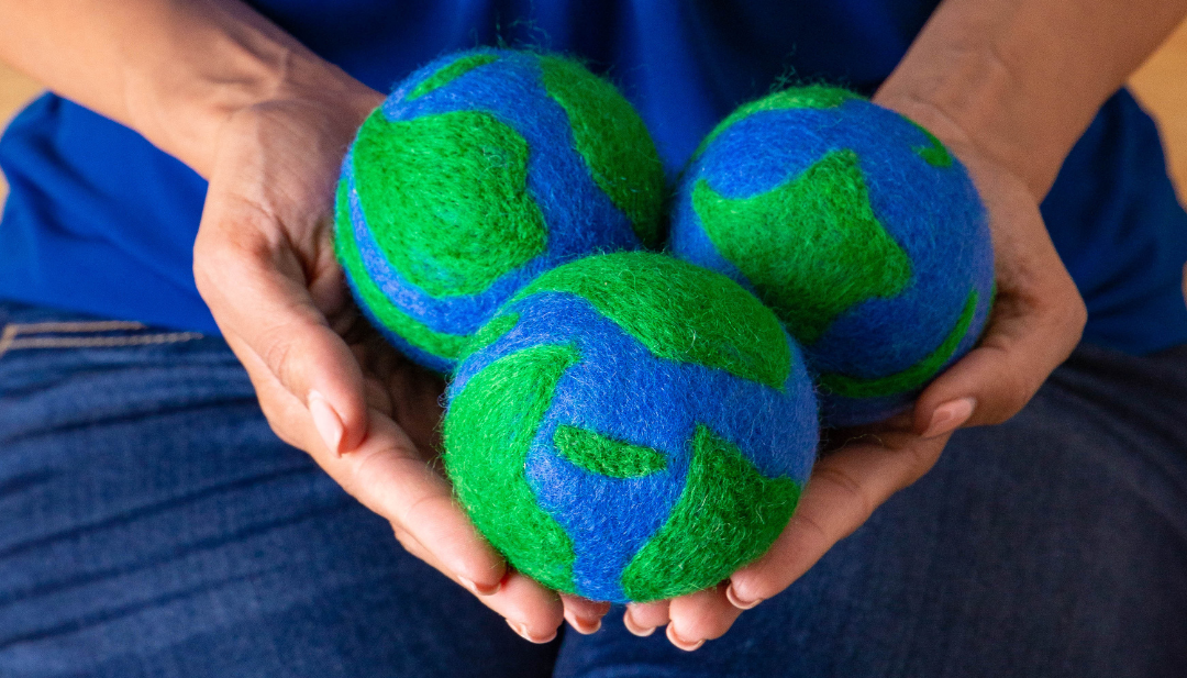 a person holds 3 green and blue Earth patterned wool dryer balls in their hands