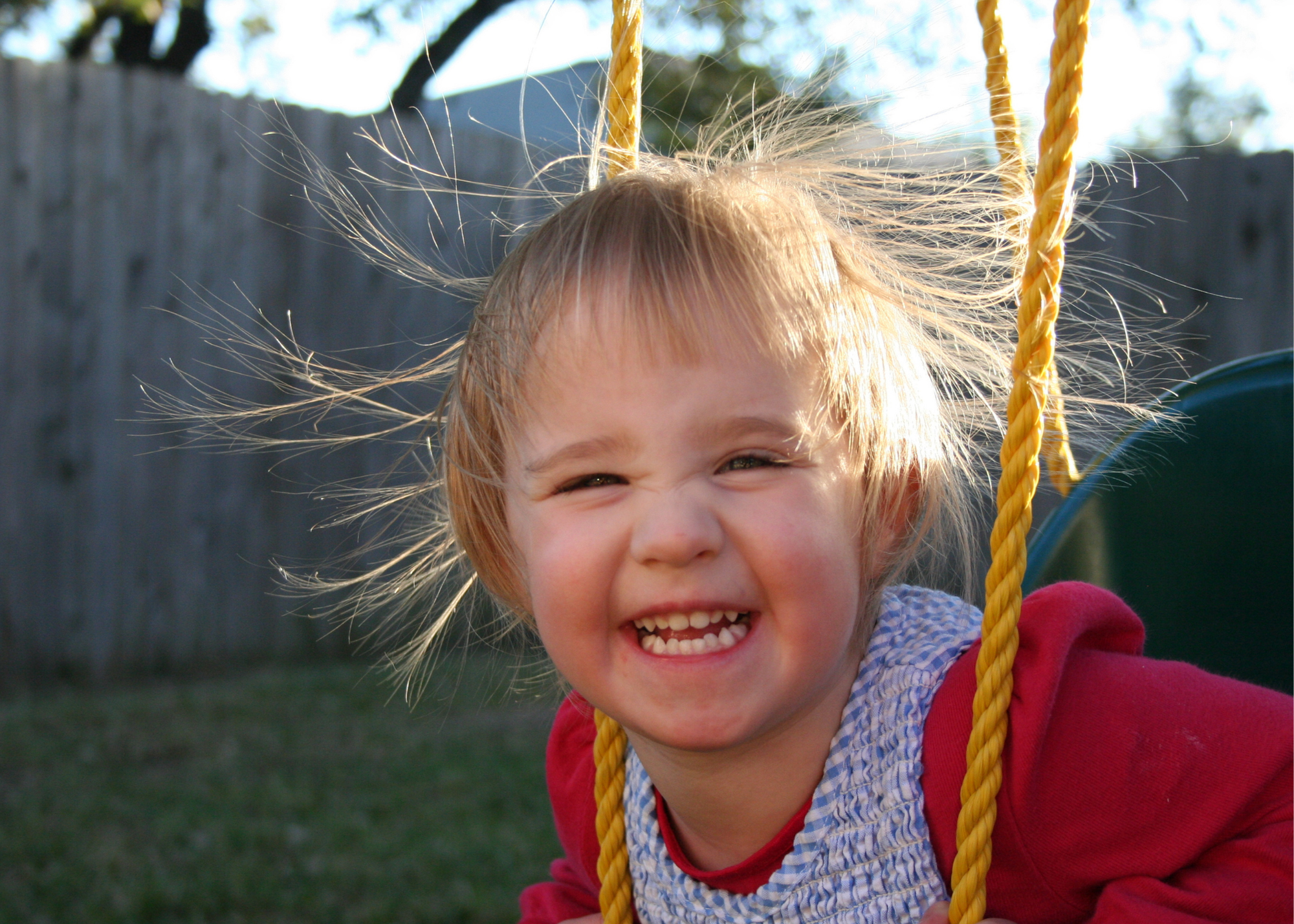 a smiling child on a swing with static hair