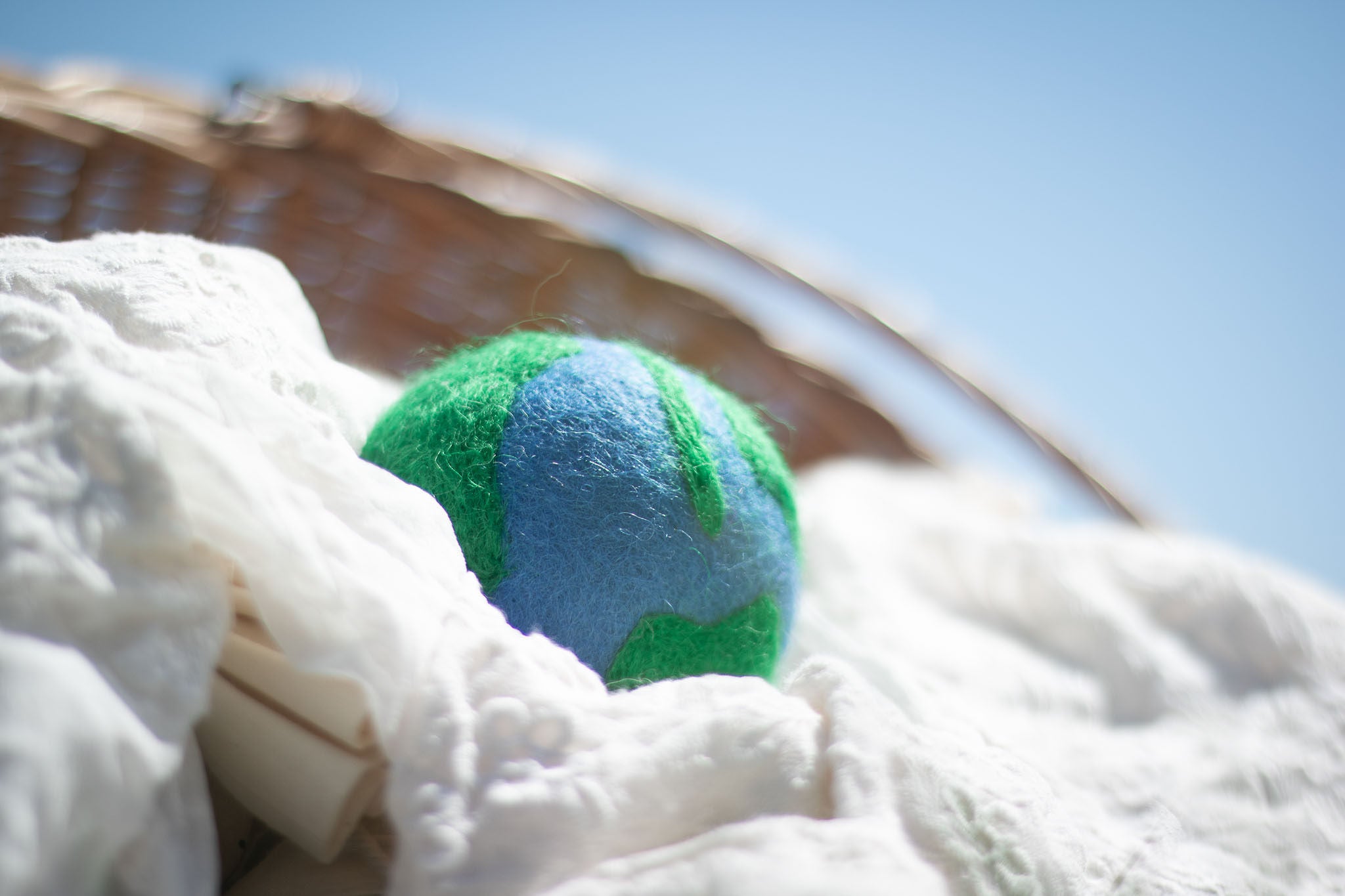 a dryer ball with a blue and green earth pattern inside a wicker basket with white sheets